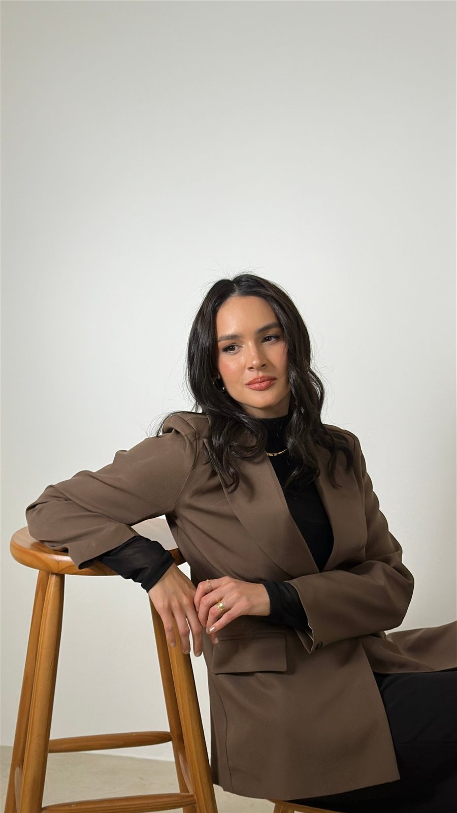 Dra. Julianna Munilla sentada, de blazer marrom, em fundo claro de estúdio